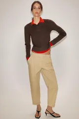 Jersey de punto con efecto doble, cuello subido y manga larga. Presenta un diseño en color marrón con detalles en rojo vibrante en el cuello, puños y ruedo. Cuenta con cierre frontal parcial mediante botones.