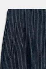 Pantalón de tiro alto y corte slim fit, color azul marino con diseño de rayas diplomáticas. Es de largo tobillero, cuenta con bolsillos delanteros de vivo y costuras marcadas en el delantero y la espalda. Cierre frontal con cremallera, botón interior y gancho metálico.