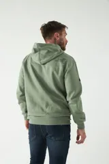 Buzo canguro de felpa color verde militar con estampado en la espalda con el logo de la marca Brookfield. Tiene capucha con cordones ajustables y bolsillo canguro.