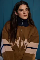 Campera tejida de punto con cierre frontal completo y cuello alto. Presenta un diseño con patrón de rombos en la parte central y franjas horizontales en las mangas.