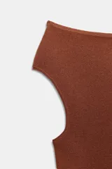 Body de tejido liso color terracota, con escote recto que deja los hombros descubiertos y mangas cortas. Cierre inferior con botones a presión.