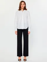 Camisa blanca de manga larga con cuello clásico y cierre frontal de botones. Presenta detalles bordados florales tono sobre tono en la zona de los hombros y el pecho.