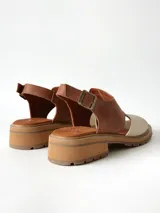 Sandalias de cuero combinadas en color marrón y crudo, con suela track y taco bajo. Tienen tira ajustable con hebilla en el talón.