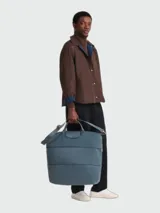 Bolso de viaje Longchamp modelo Le Pliage One, de diseño minimalista y funcional en color azul grisáceo. Cuenta con asas cortas, correa ajustable para el hombro y cierre superior con solapa de botón a presión.