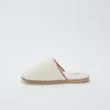 Pantuflas abiertas de pelo sintético color beige con suela marrón.