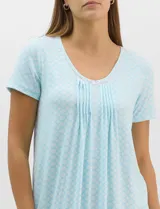 Camisón corto de corte evasé celeste con estampado geométrico, mangas cortas y amplio escote redondo. Presenta detalle de puntilla calada en el contorno del cuello con pequeño moño decorativo en el centro y fruncidos frontales.