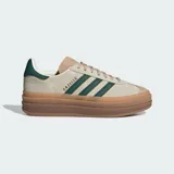 Championes Adidas Gazelle Bold color beige con las tres tiras clásicas en verde oscuro y suela de goma marrón con plataforma.