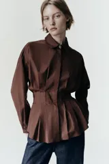 Camisa de manga larga en color celeste claro, confeccionada en tejido de popelín. Presenta cuello solapa, cintura entallada con detalle de pliegues y cierre frontal con botones ocultos por tapeta.
