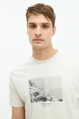 Remera de manga corta color beige con estampado fotográfico en el pecho. Presenta un corte regular y cuello redondo.