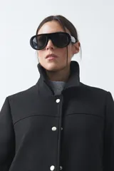 Tapado corto de paño color marrón, con diseño recto, cuello camisero y cierre frontal con broches metálicos. Cuenta con bolsillos frontales.