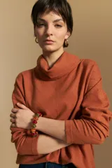 Polera de tejido de punto color naranja con cuello alto de caída relajada y diseño de líneas en relieve. Presenta una silueta holgada con hombros caídos y mangas largas.