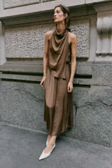 Vestido midi satinado de color marrón, con cuello fluido y diseño sin mangas. Presenta un cierre en la espalda con botones y una falda fluida con sutiles pliegues.
