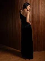 Vestido largo de terciopelo con diseño de un solo hombro y textura plisada. Presenta un corte ajustado en la cintura y una caída fluida hasta el suelo.