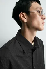 Camisa negra de corte relaxed fit, con cuello solapa y cierre frontal de botones, manga larga con puños abotonados y sutil patrón geométrico en jacquard.