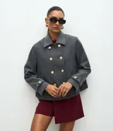 Saco corto de corte regular confeccionado en polivelour gris, con cuello inglés, cierre frontal de doble abotonadura con botones dorados y mangas largas con detalle de trabas en los puños.