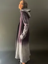 Tapado largo de lana merino color gris oscuro con teñido degradado en gris claro en ruedo, mangas y capucha. Tiene corte recto, bolsillos laterales y cierre cruzado con broches a presión ocultos en los hombros.