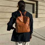 Mochila de eco cuero color suela, de diseño amplio con múltiples bolsillos externos con cierre y tiradores largos. Cuenta con asa superior y correas ajustables.