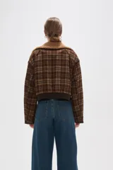 Campera corta de estilo bomber con estampado a cuadros en tonos marrones. Presenta cuello de corderito sintético, cierre frontal con cremallera, dos bolsillos frontales con solapa y puños y ruedo de tejido elástico acanalado.