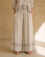 Pantalón de lino color beige, de corte wide leg y tiro alto, con cintura elástica, bolsillos laterales y detalle de franja calada en el bajo.