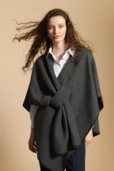 Poncho gris oscuro de tejido suave con diseño envolvente y cierre frontal anudado. Presenta bordes con costuras decorativas en contraste de color negro.