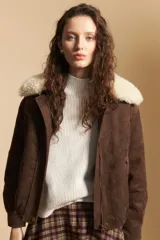 Campera de gamuza color marrón con cuello de corderito sintético en color crema. Presenta cierre frontal, bolsillos laterales con broches metálicos y puños rectos.