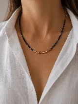 Collar de cuentas negras facetadas con una sección central de pequeñas piezas cilíndricas doradas.