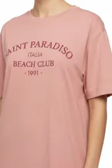 Remera de manga corta color rosado, con diseño holgado, cuello redondo a la base y estampa frontal en tono bordó con la inscripción "Saint Paradiso Italia Beach Club 1991".