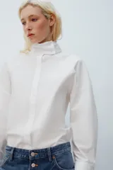 Camisa amplia blanca de cuello alto y manga larga, con cierre frontal de botones.