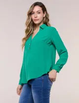 Blusa verde de calce holgado y caída fluida, confeccionada en tejido tipo crepé. Cuenta con cuello camisero con solapa, escote en V y cierre parcial al frente con tres botones metálicos. Las mangas son largas con puños abotonados.