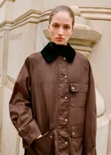 Parka color marrón con efecto encerado, diseño recto y manga larga. Cuenta con cuello camisero de pana, cierre frontal de cremallera y botones a presión, múltiples bolsillos de parche con solapa y forro interior.