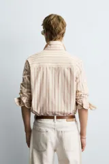Camisa de corte relajado confeccionada en tejido con mezcla de viscosa, con diseño de rayas verticales en tonos beige y marrón. Presenta cuello solapa, cierre frontal de botones, manga larga con puños abotonados y un bolsillo en el pecho.