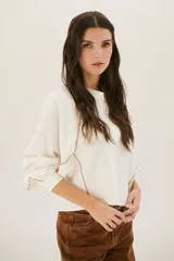 Buzo negro de corte cropped con mangas largas abullonadas y costuras a la vista en color blanco.