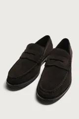 Mocasín de vestir para hombre, fabricado en piel con acabado en serraje de color azul marino. Presenta un diseño clásico con detalle de antifaz en el empeine, horma redonda, costuras visibles en el contorno y una suela sutil con ligero tacón.