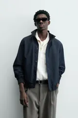 Cazadora azul marino de corte regular fit, confeccionada en tejido técnico repelente al agua. Presenta cuello subido, manga larga, bolsillos de vivo en cadera, bolsillo interior y acabados en rib en puños y bajo. Cierre frontal de cremallera oculta por solapa con botones a presión.