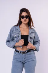 Campera de jean cropped con tachas plateadas distribuidas en el frente, hombros y mangas. Presenta un diseño con bordes deshilachados, cuello clásico y cierre frontal con botones metálicos.