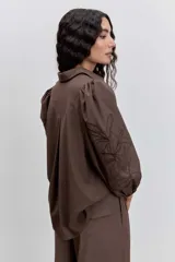 Camisa de color marrón con cuello clásico, mangas abullonadas y detalle de bordado floral en una de las mangas.