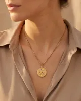 Collar de acero con baño de oro, compuesto por una cadena de eslabones finos y un dije circular con diseño de árbol de la vida grabado, decorado con pequeñas circonias de colores.