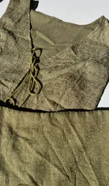 Conjunto de dos piezas color verde oliva con textura arrugada. Incluye un chaleco sin mangas con cierre frontal de lazos y una minifalda ajustada.