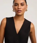 Chaleco negro de sastre, corte slim, sin mangas, con escote en V profundo y cierre frontal de cuatro botones. Presenta un bolsillo o falso bolsillo a la altura del pecho y está forrado.