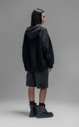 Hoodie oversize color negro, confeccionado en frisa gamuzada de algodón. Presenta capucha forrada en microfibra, mangas raglán y un bolsillo frontal tipo canguro con un bolsillo pequeño superpuesto con solapa.