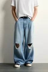Jeans baggy fit de corte holgado en denim de algodón celeste, con tiro medio, cinco bolsillos, roturas en las rodillas y cierre frontal con cremallera y botón.