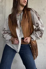 Chaleco de gamuza color camel forrado, con ribetes decorados con tachas metálicas y tiras colgantes con flecos en el lateral.