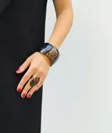 Pulsera rígida de diseño ancho, elaborada en resina de alta calidad con un acabado que combina secciones en color negro sólido y estampado tipo carey.