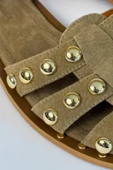 Sandalias planas de gamuza color tostado, con múltiples tiras decoradas con tachas metálicas doradas semiesféricas. Cuenta con una tira ajustable en el tobillo con hebilla metálica.