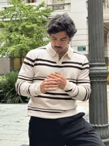 Buzo tejido de punto con diseño a rayas horizontales en color beige y marrón. Presenta cuello tipo polo con cierre frontal parcial y puños acanalados.