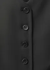 Chaleco de sastre color negro, con cuello en pico y cierre frontal de botones. Presenta un diseño recto, sin mangas y cuenta con dos bolsillos de ribete en la parte delantera.