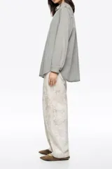 Pantalón de corte barrel color negro, con tiro medio, cierre frontal con botón y cremallera, cinco bolsillos y detalle de tachas metálicas a lo largo de las costuras laterales.