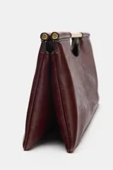Bolso de mano de diseño estructurado en color bordó, con asa rígida dorada integrada en la parte superior y cierre magnético.