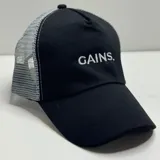 Gorro trucker negro con frente de tela y parte trasera de rejilla gris. Tiene visera curva y bordado frontal con la palabra "GAINS." en blanco.