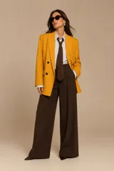 Chaqueta cruzada color mostaza con cierre de botones negros, bolsillos con tapa y detalle de botones en los puños.